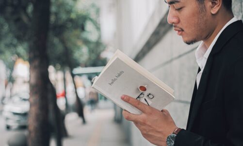 Mężczyzna w marynarce czyta książkę pt. „hello, habits” na ulicy.
