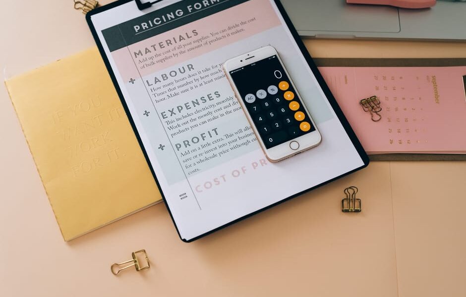 Smartfon z włączonym kalkulatorem leżący na formularzu wyceny produktów z materiałami biurowymi.